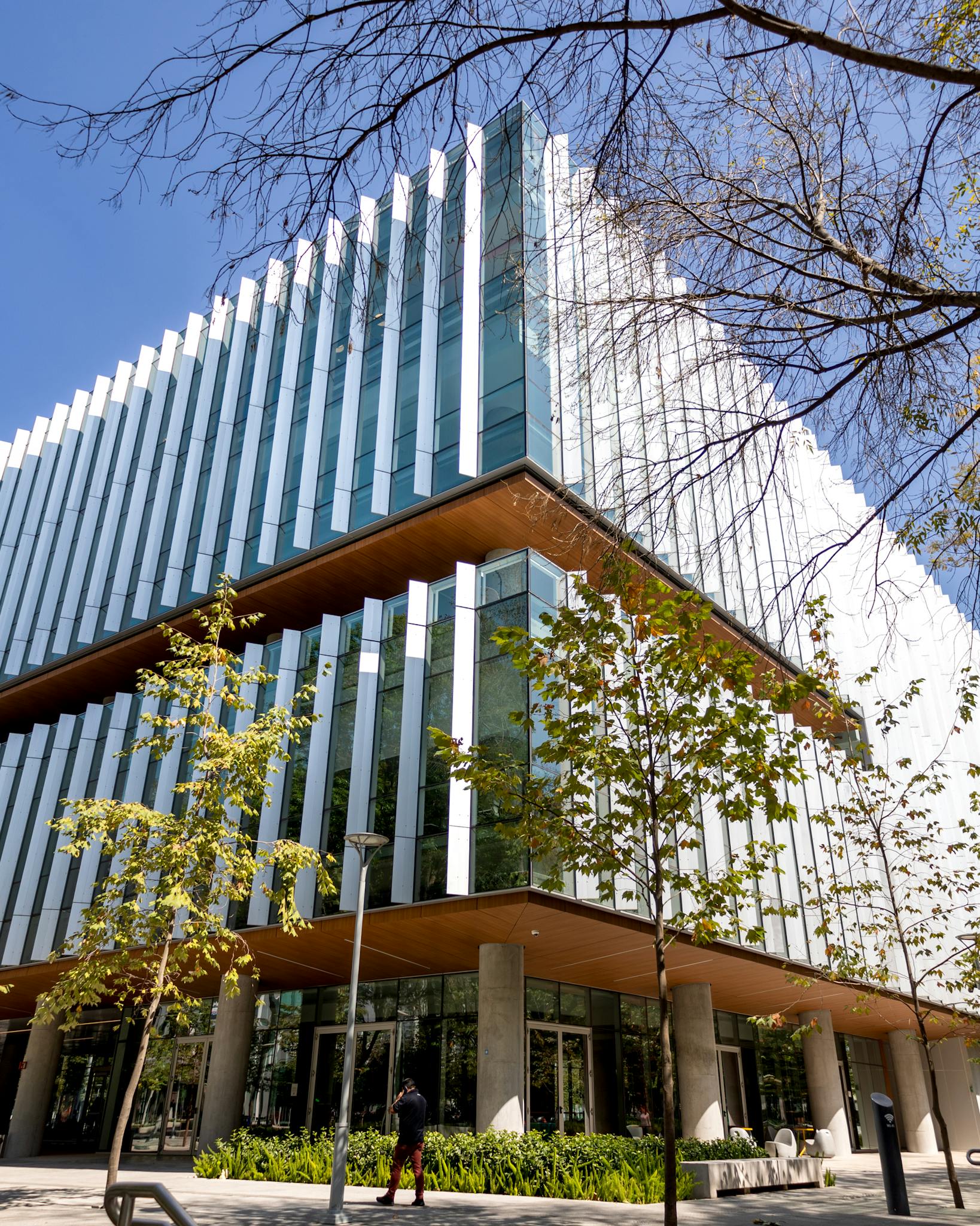 Contemporary glass-fronted office building with trees in urban setting on a sunny day.