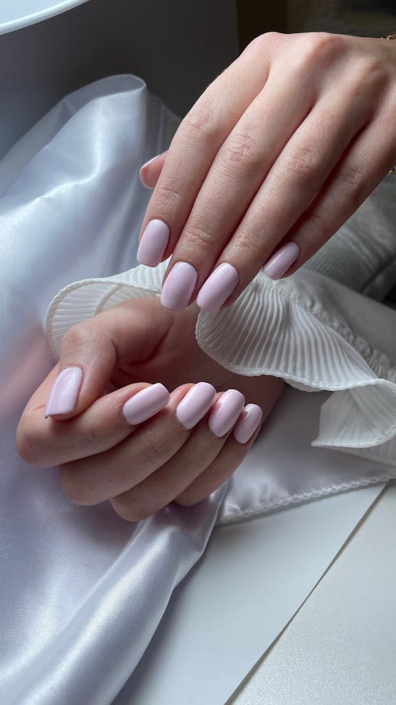 Close-up of hands with pink nail polish resting on white silk fabric, showcasing elegance.